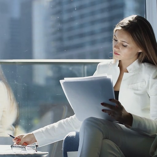 A_woman_in_a_white_jacket_reviews_paperwork_near_a_window,_urban_skyline_visible_outside_ours