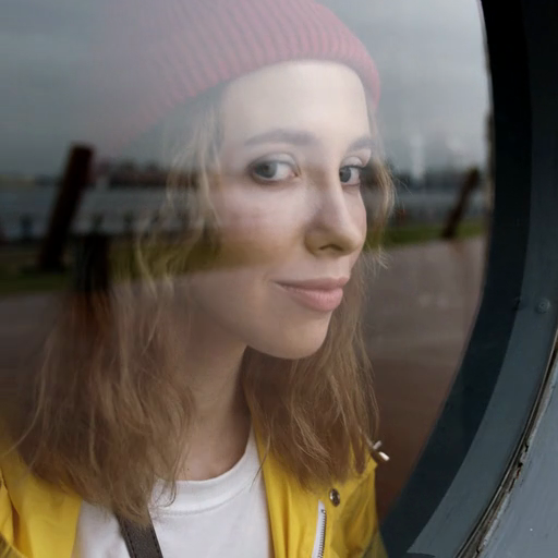 A_woman_wearing_a_red_beanie_looking_out_through_a_round_window_ours
